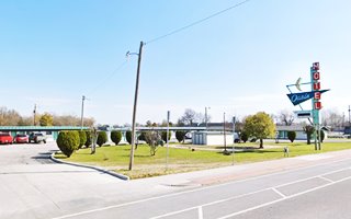 motel behind a neon sign reading MOTEL in red panels a boomerang, and blue triangle with OASIS, Route 66 runs in front