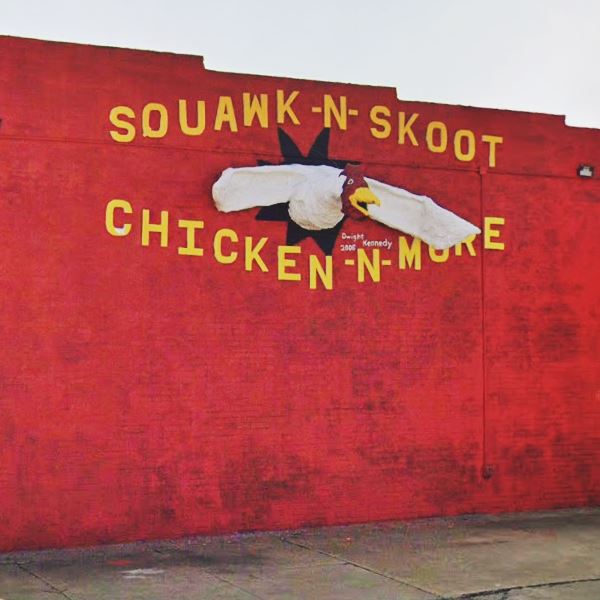 white chicken with wings extended sticking out of brick wall painted red