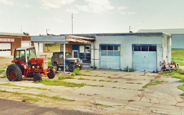 slowly decaying vintage gas station with tractors parked next to it