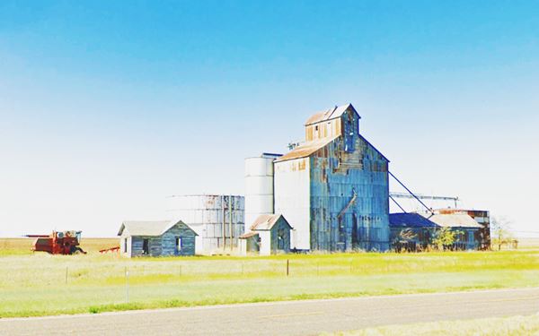 grain elevators and empty buildings in a field by Route 66